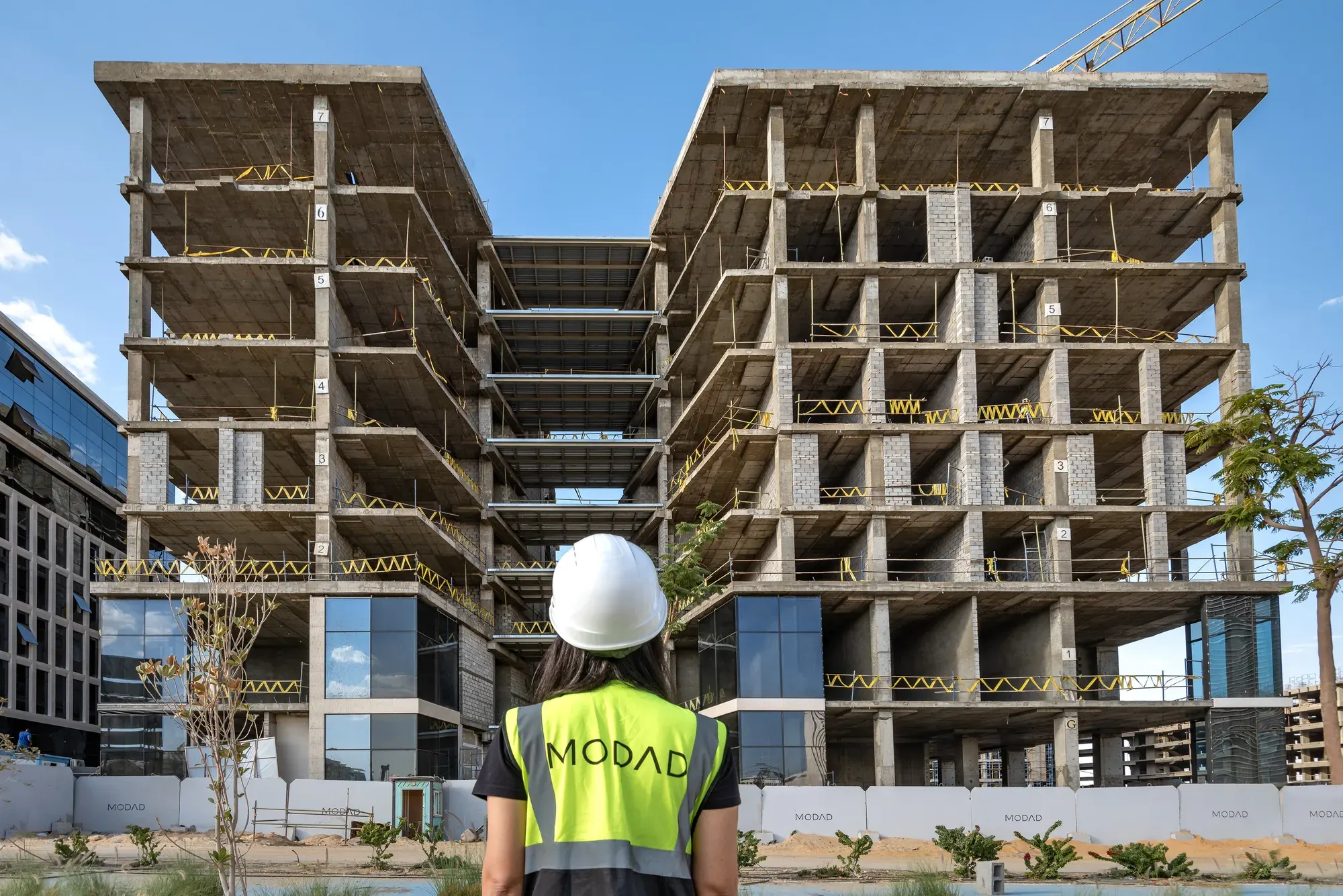 Guest in a white hard hat and MODAD vest facing the SECTOR building
